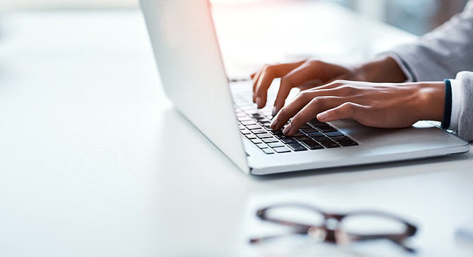 Eine junge Frau sitzt am Laptop und tippt auf der Tastatur, zu sehen sind nur ihre Hände.