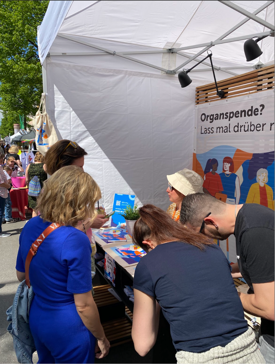 Das Bild zeigt einen belaufenen Stand des BIÖG Organspende und Menschen, die Organspendeausweise unterschreiben.